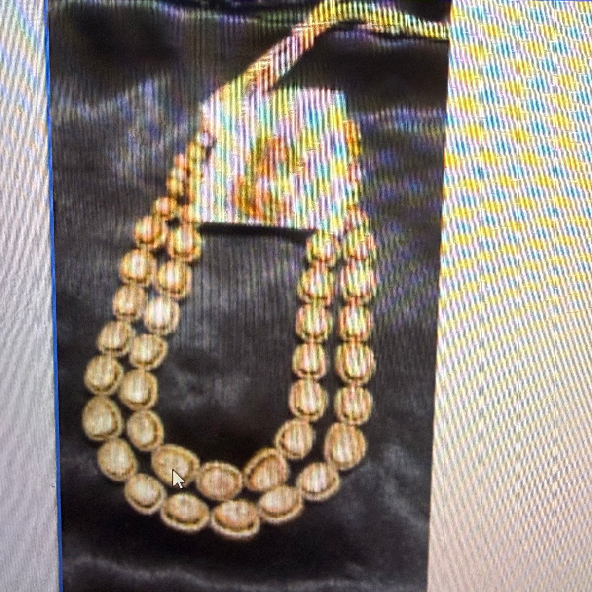 A double-strand traditional Indian necklace with gold-toned circular stones and a central iridescent pendant, displayed on a black satin fabric.