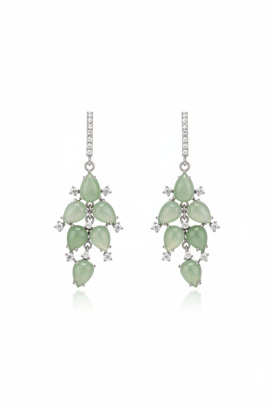A pair of dangling earrings with light green floral charms and silver-toned metal, displayed on a small white card on a dark surface. The photo appears to be a screenshot of a computer monitor showing a product photo.