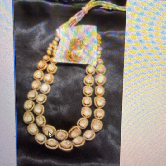 A double-strand traditional Indian necklace with gold-toned circular stones and a central iridescent pendant, displayed on a black satin fabric.