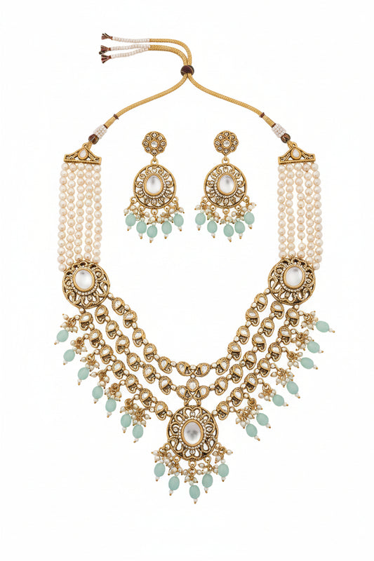 An ornate traditional necklace with gold-toned filigree, white pearl-like beads, and light blue-green stone accents, displayed on a dark satin fabric.