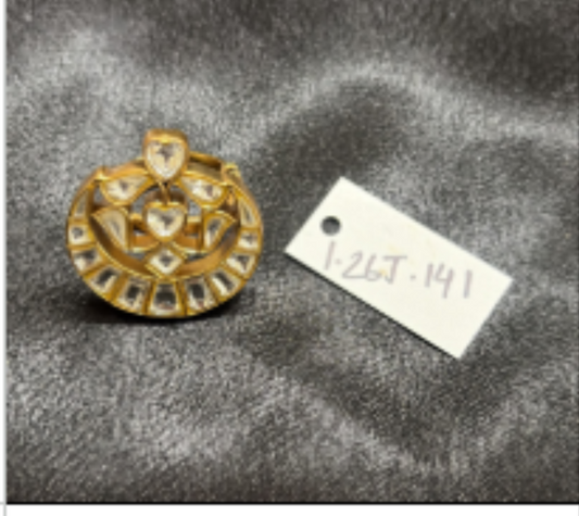 A product photo of a gold-toned circular pendant or medallion with a central cutout, placed on a gray textured surface next to a small handwritten tag. The photo is captured within a browser window showing a spreadsheet, with page numbers and browser tabs visible.
